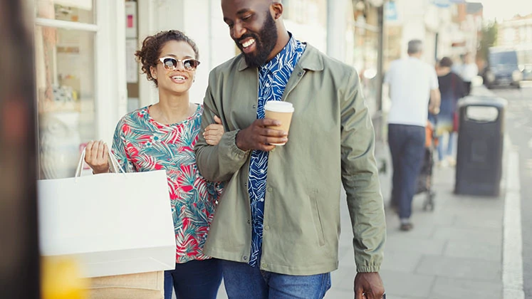 Smiling young couple coffee shopping bags walking along storefro