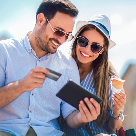 Smiling couple outside looking at a computer holding a credit card while enjoying an ice cream cone.