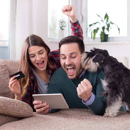 Young excited couple with dog together on floor looking at the computer.