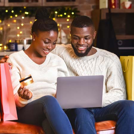 Young couple sitting on couch surrounded by shopping bags while shopping on computer.