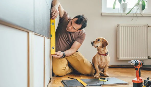 A man holds a level while doing kitchen renovations. His dog watches on in earnest.