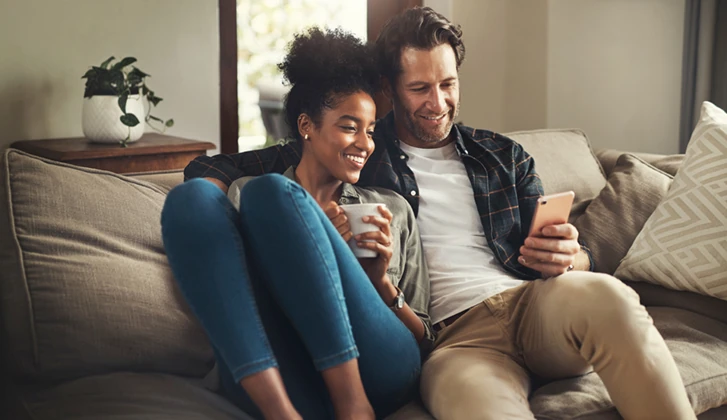 Shot of a happy young couple using a digital tablet while relaxing on a couch in their living room at home.