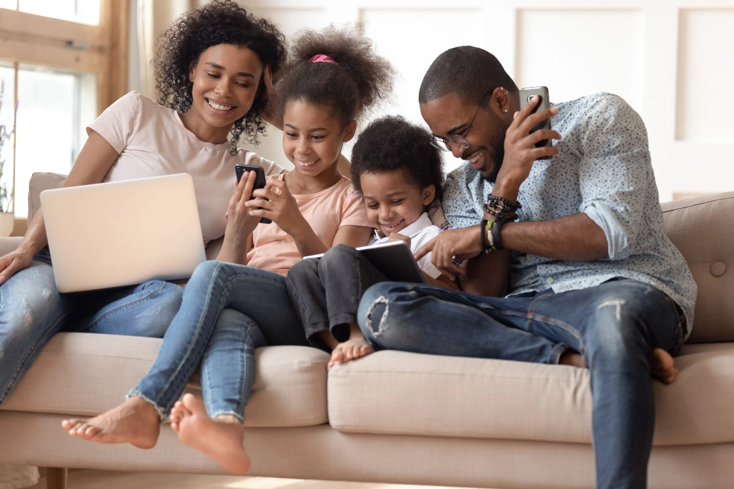 Family sitting on living room couch with laptop, tablet and smart phones reviewing safe online practices