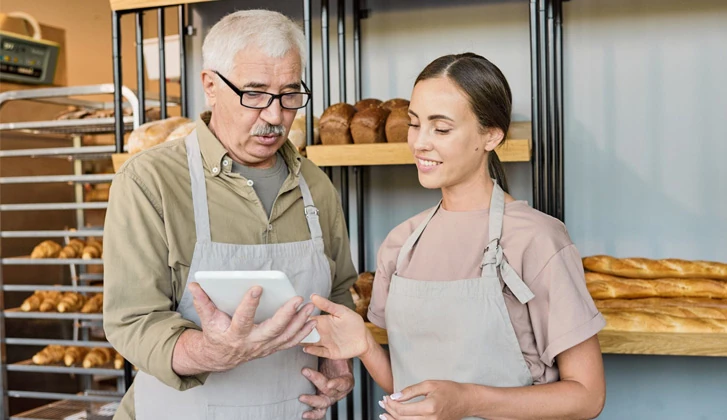 Elderly man and younger woman with aprons on behind a bakery counter