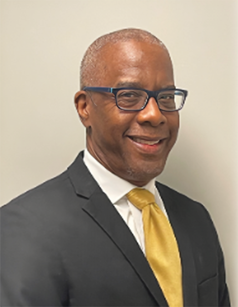 Professional headshot of Theron Green with a yellow tie and a neutral background.