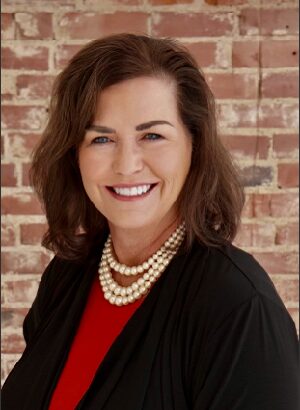 professional headshot of melanie ahrens smiling before a brick background