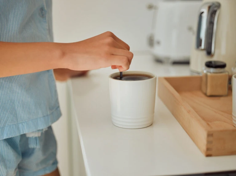 A girl hands stirring coffee in kitchen.