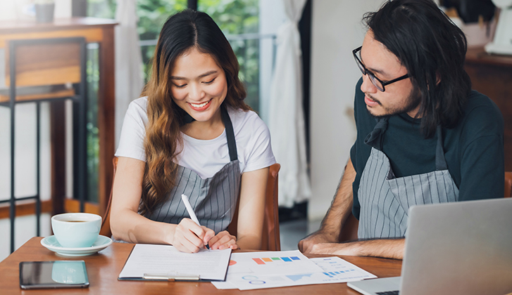 young man and woman doing business paperwork at a table with aprons